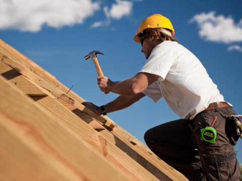 man-with-yellow-hard-hat-and-hammer-on-rooftop